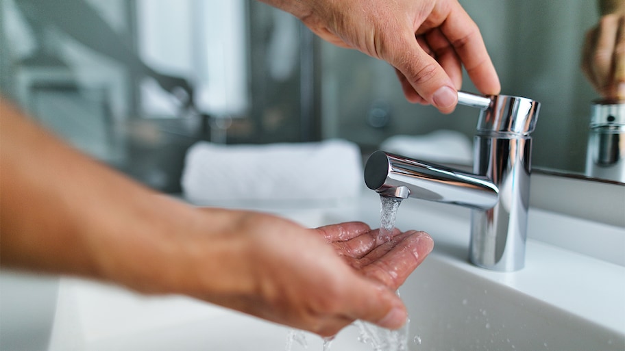 A hand lifting a sink faucet and holding hand under stream of water