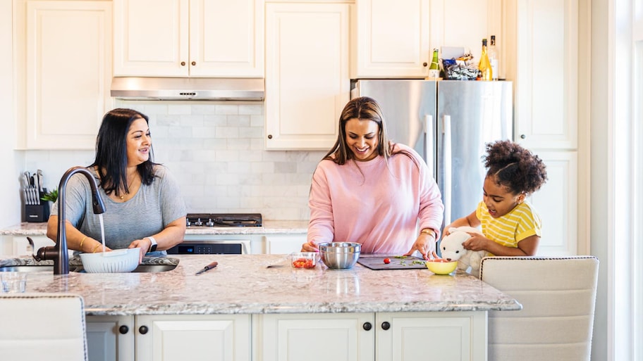 A girl playing with teddy bear while smiling mother and grandmother at kitchen island