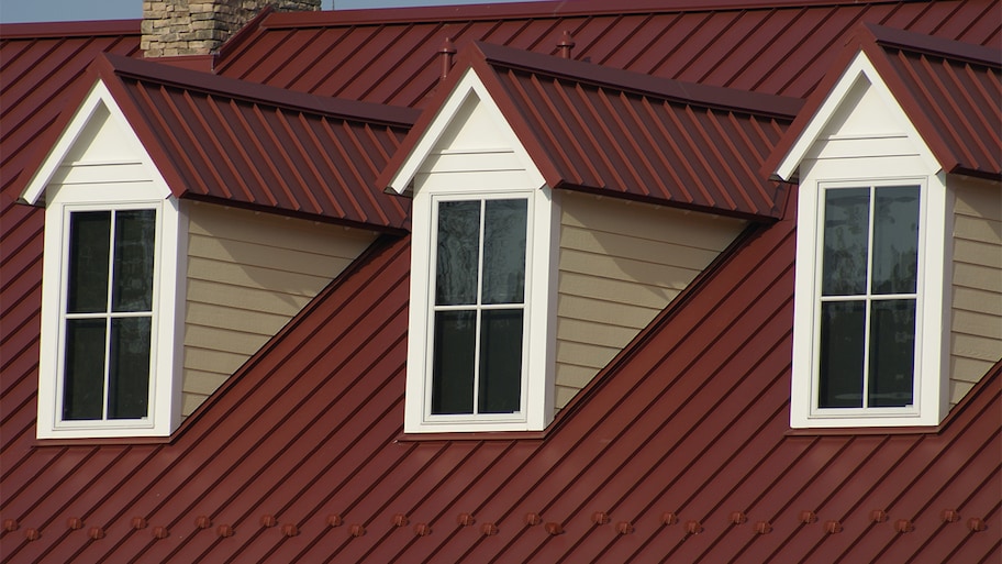 A home's roof with red shingles and windows