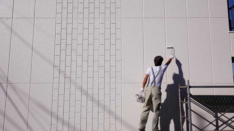 A man painting a high wall on a commercial building