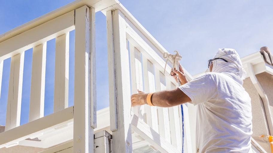 A person in protective gear painting a deck white