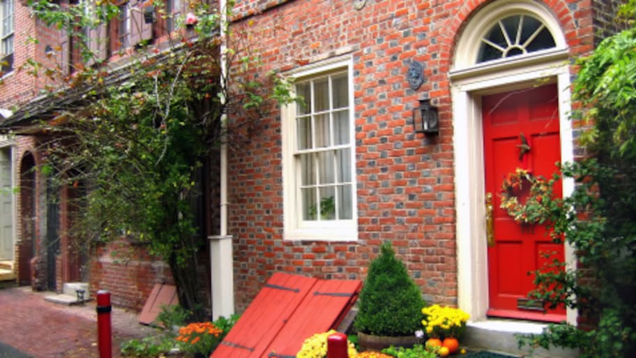 Red storm shelter door in front of a brick house