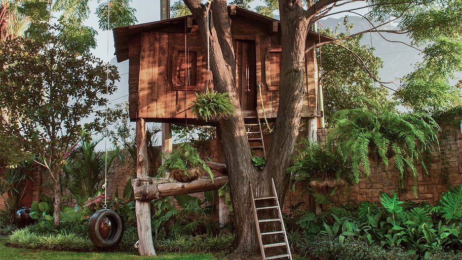 treehouse in lush backyard with a ladder leading up to it and a tire swing hanging from the tree