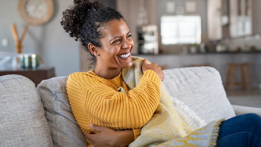 A woman covered in a blanket laughing while sitting on the sofa