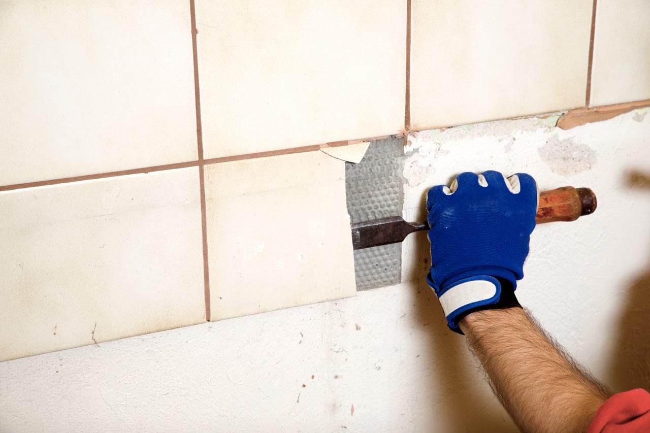 Close-up of a worker removing old tiles from a wall